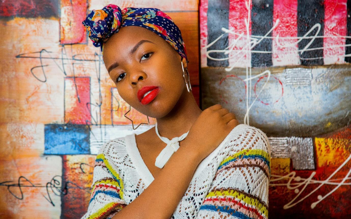 A woman with a colorful bandana posing against a wall