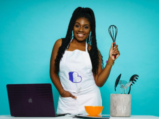 An African American woman holding a whisk in front of a laptop