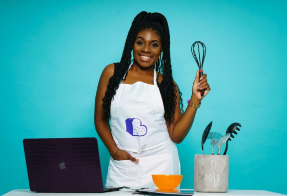 An African American woman holding a whisk in front of a laptop