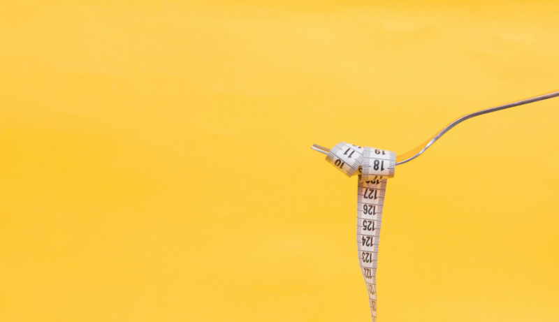 A fork with a measuring tape wrapped around it against a yellow background.