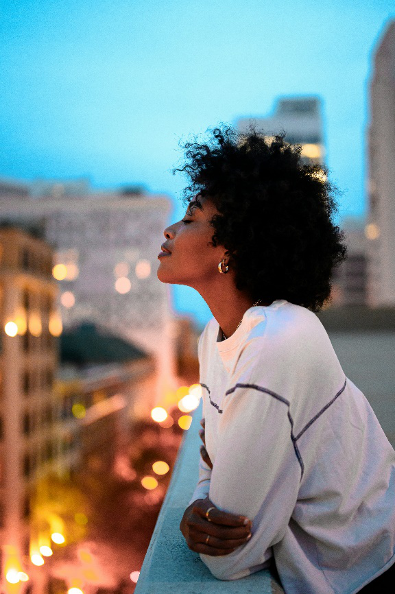 Woman reflecting on a city rooftop at dusk.