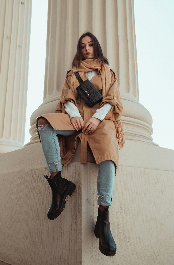 Woman in layered tan coat, jeans, and black boots for a cozy fall look.