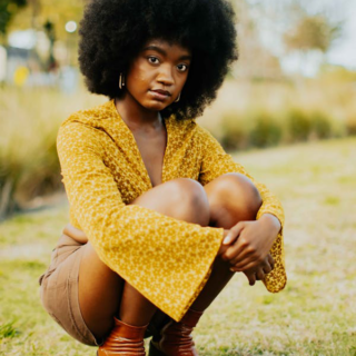 a young woman in a mustard yellow top sitting outdoors.