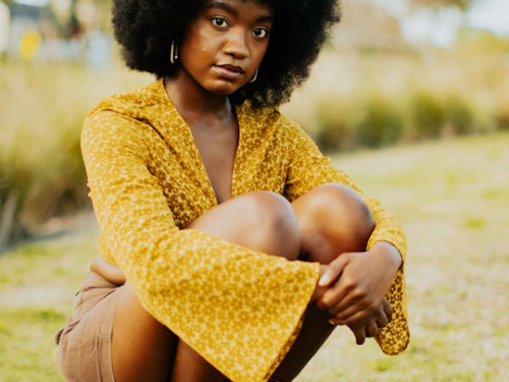 a young woman in a mustard yellow top sitting outdoors.