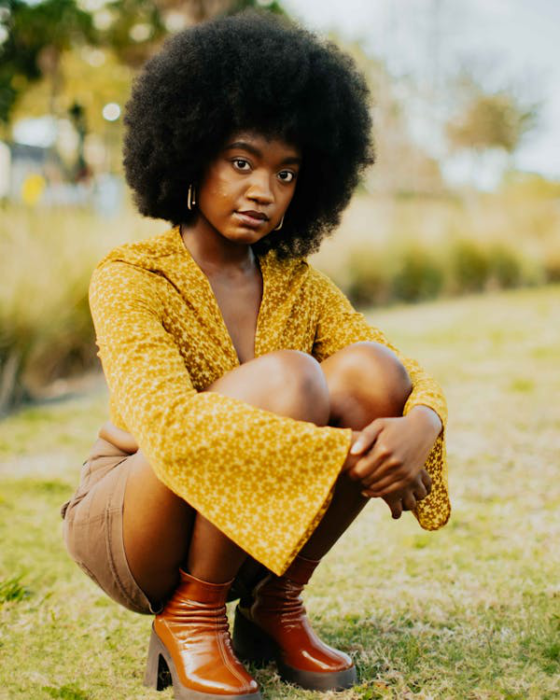 a young woman in a mustard yellow top sitting outdoors.