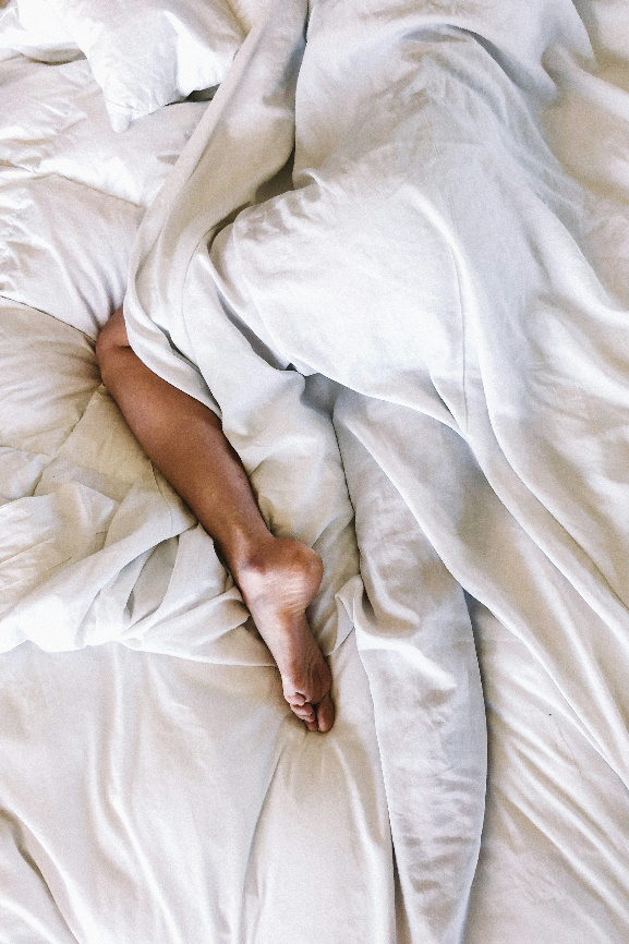 A single foot peeking out from under cozy white blankets.