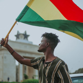 Man holding Ghana flag in front of historic landmark