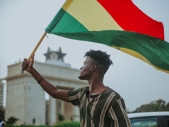 Man holding Ghana flag in front of historic landmark