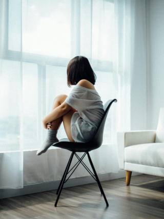 Woman sitting on a chair by the window, looking outside thoughtfully.