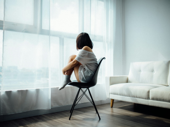 Woman sitting on a chair by the window, looking outside thoughtfully.