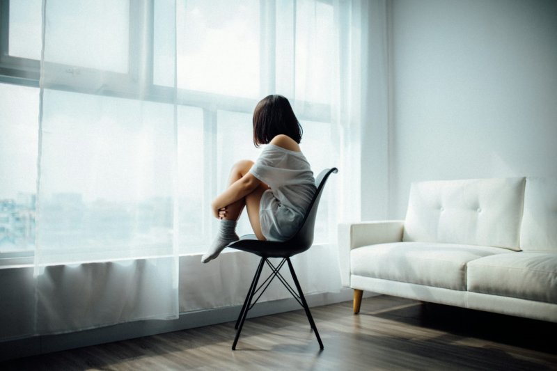 Woman sitting on a chair by the window, looking outside thoughtfully.