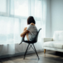 Woman sitting on a chair by the window, looking outside thoughtfully.