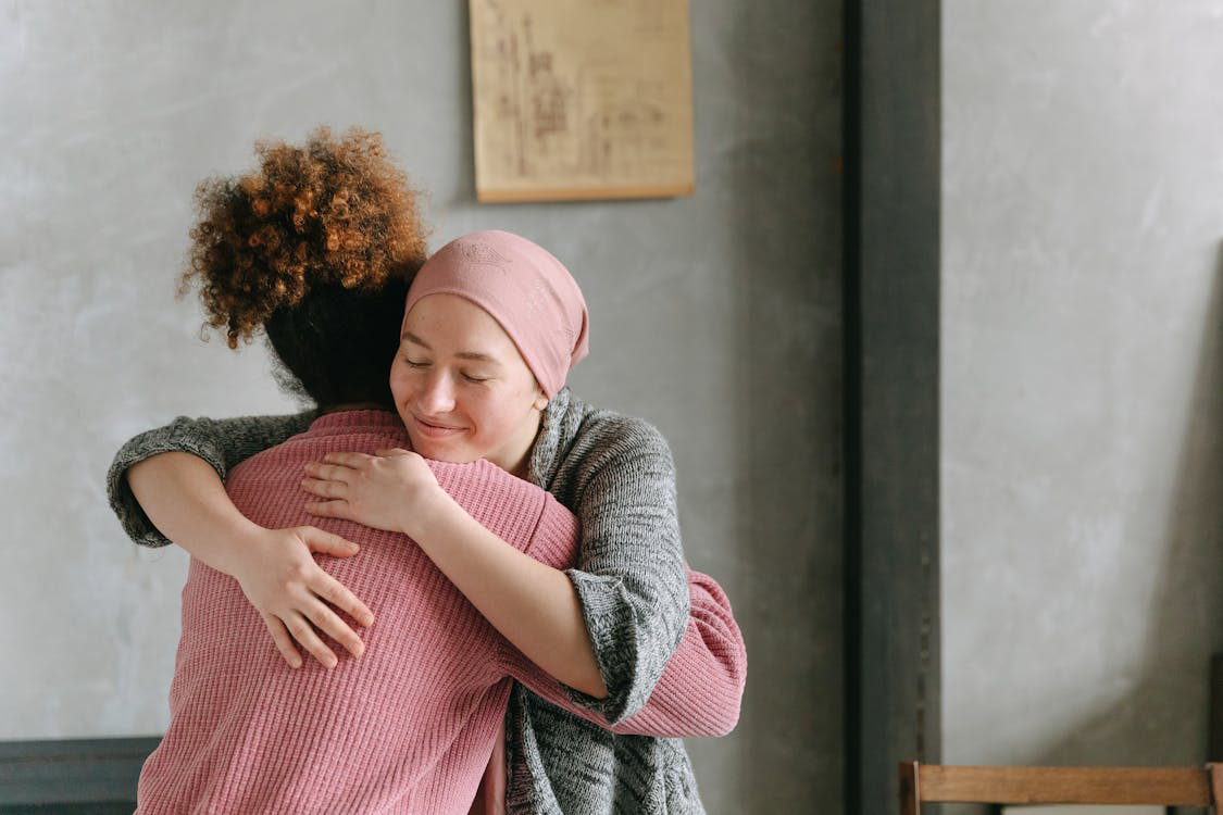 Woman in a headscarf embracing a friend for support.