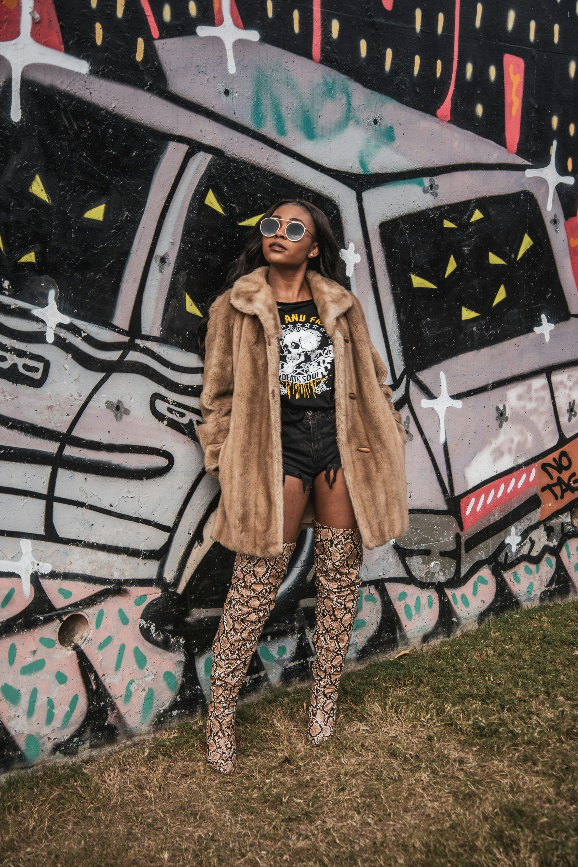 Woman in a fur coat and snake-print boots in front of a graffiti-covered wall.