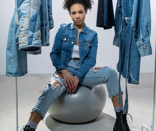 Woman wearing a denim jacket and pants, posing confidently near a clothing rack.