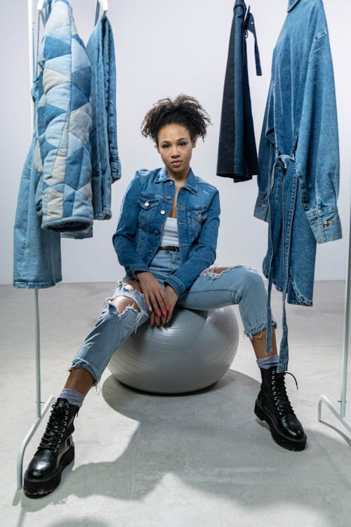 Woman wearing a denim jacket and pants, posing confidently near a clothing rack.