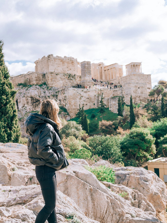 A traveler in a black winter jacket overlooking the historic Acropolis in Athens, Greece.