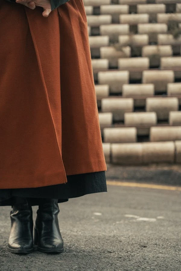 A stylish woman wearing ankle boots and a skirt, layered with a chic coat for a winter-to-spring transition look.