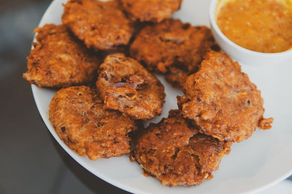 Golden-brown conch fritters served with a tangy dipping sauce on a white plate.