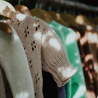 A collection of lightweight knit sweaters neatly hung on a clothing rack in neutral and pastel shades.