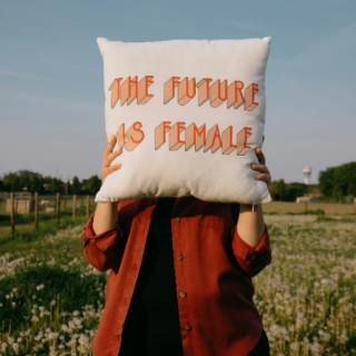 Woman holding pillow with “The Future is Female” written on it in a field