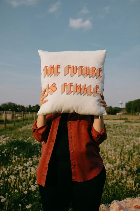 Woman holding pillow with “The Future is Female” written on it in a field
