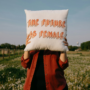 Woman holding pillow with “The Future is Female” written on it in a field
