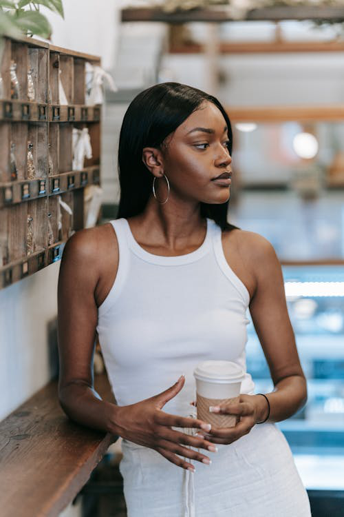 Stylish woman in a white tank top holding a to-go coffee cup