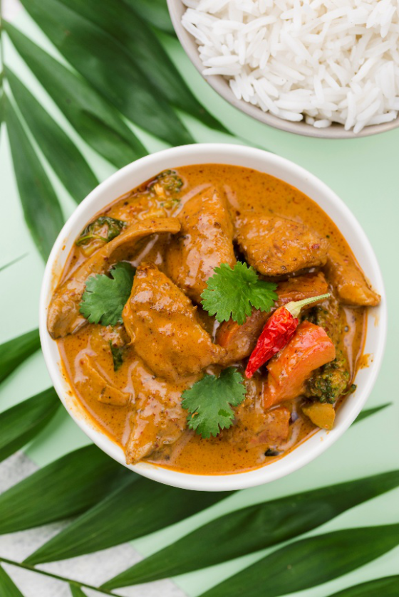 A bowl of Jamaican curry chicken with rice on a green background
