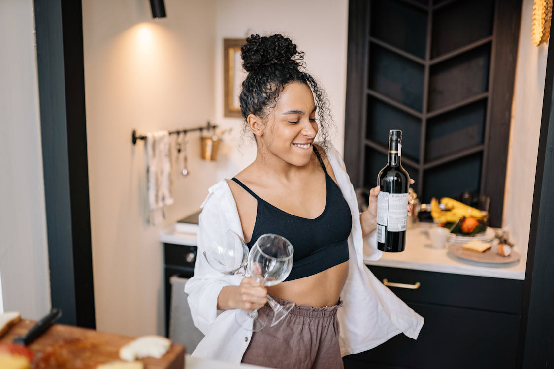 A young woman smiling and dancing in the kitchen with wine and glasses