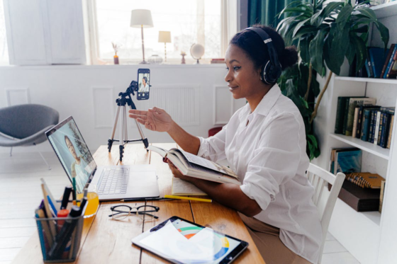A woman wearing headphones in a remote work setup with a laptop and phone