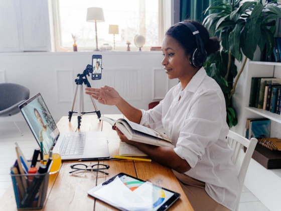 A woman wearing headphones in a remote work setup with a laptop and phone