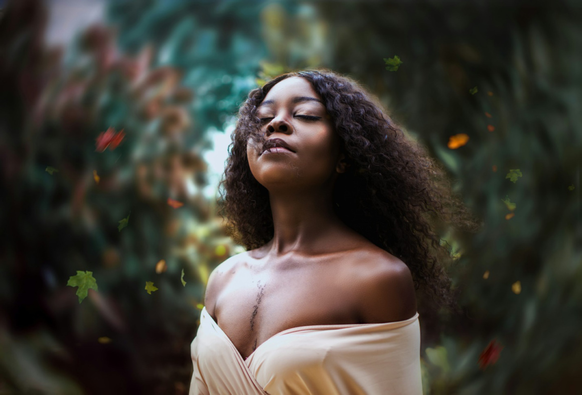 Aesthetic photo of a woman in an off-shoulder beige top, with her eyes closed, face raised upwards, and wind sweeping through her hair.