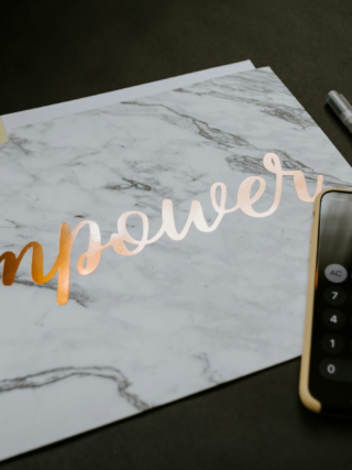 Marble notebook with the word "empower" in metallic script beside a calculator and pen on a dark desk