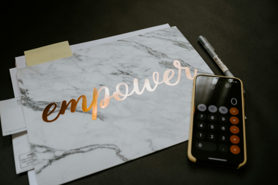 Marble notebook with the word "empower" in metallic script beside a calculator and pen on a dark desk