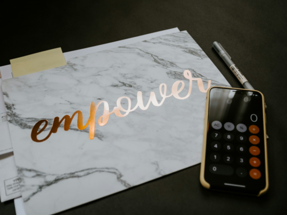 Marble notebook with the word "empower" in metallic script beside a calculator and pen on a dark desk
