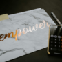 Marble notebook with the word "empower" in metallic script beside a calculator and pen on a dark desk