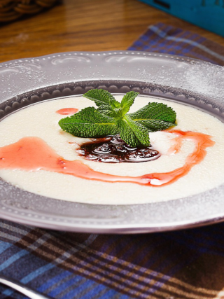 A bowl of creamy Jamaican cornmeal porridge topped with berry syrup and mint leaves on a plaid cloth.