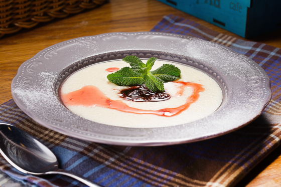 A bowl of creamy Jamaican cornmeal porridge topped with berry syrup and mint leaves on a plaid cloth.