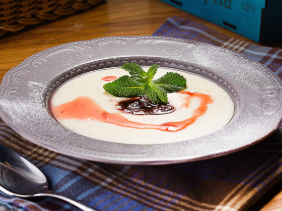 A bowl of creamy Jamaican cornmeal porridge topped with berry syrup and mint leaves on a plaid cloth.