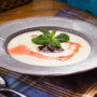 A bowl of creamy Jamaican cornmeal porridge topped with berry syrup and mint leaves on a plaid cloth.