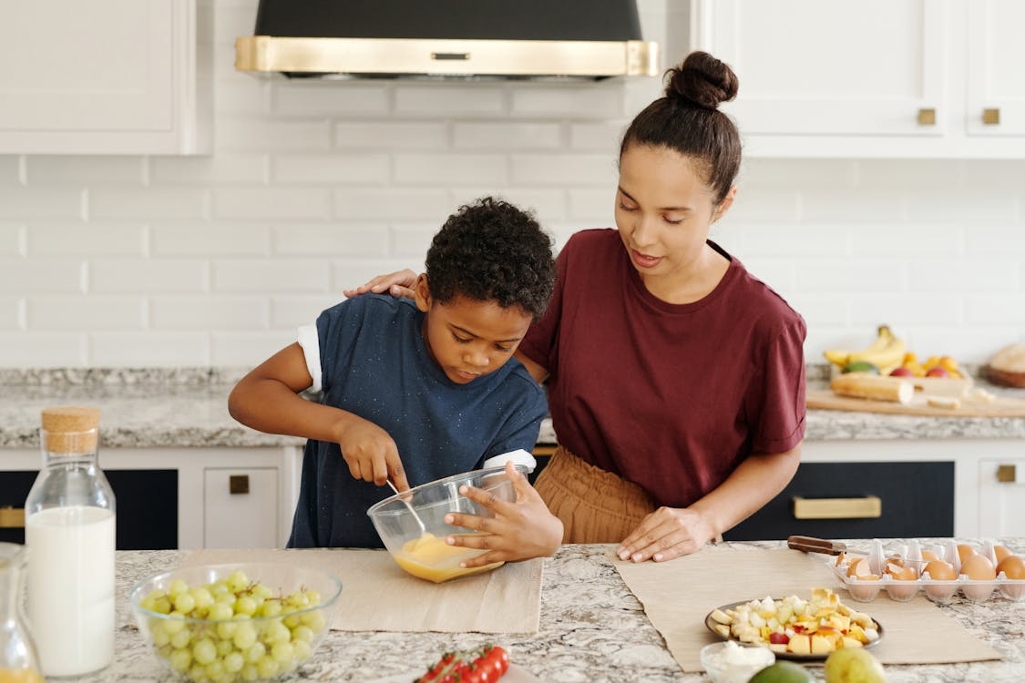 African-American mother helping her son mix ingredients in a kitchen while preparing Jamaican cornmeal porridge.