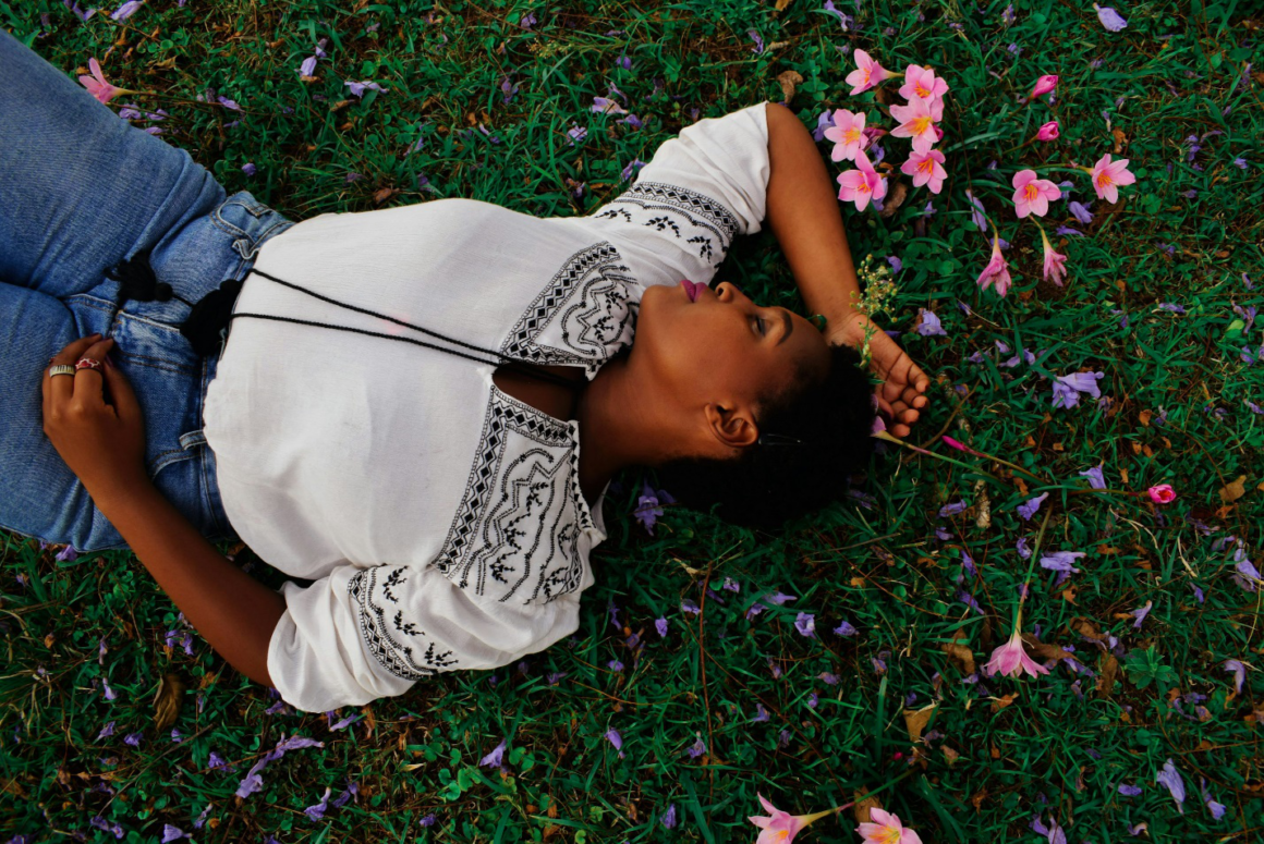 A lady lying on grass with pink flowers around her.