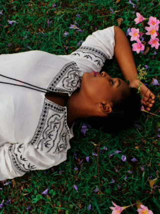 A lady lying on grass with pink flowers around her.