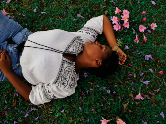A lady lying on grass with pink flowers around her.