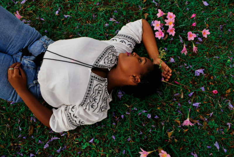 A lady lying on grass with pink flowers around her.