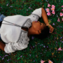 A lady lying on grass with pink flowers around her.