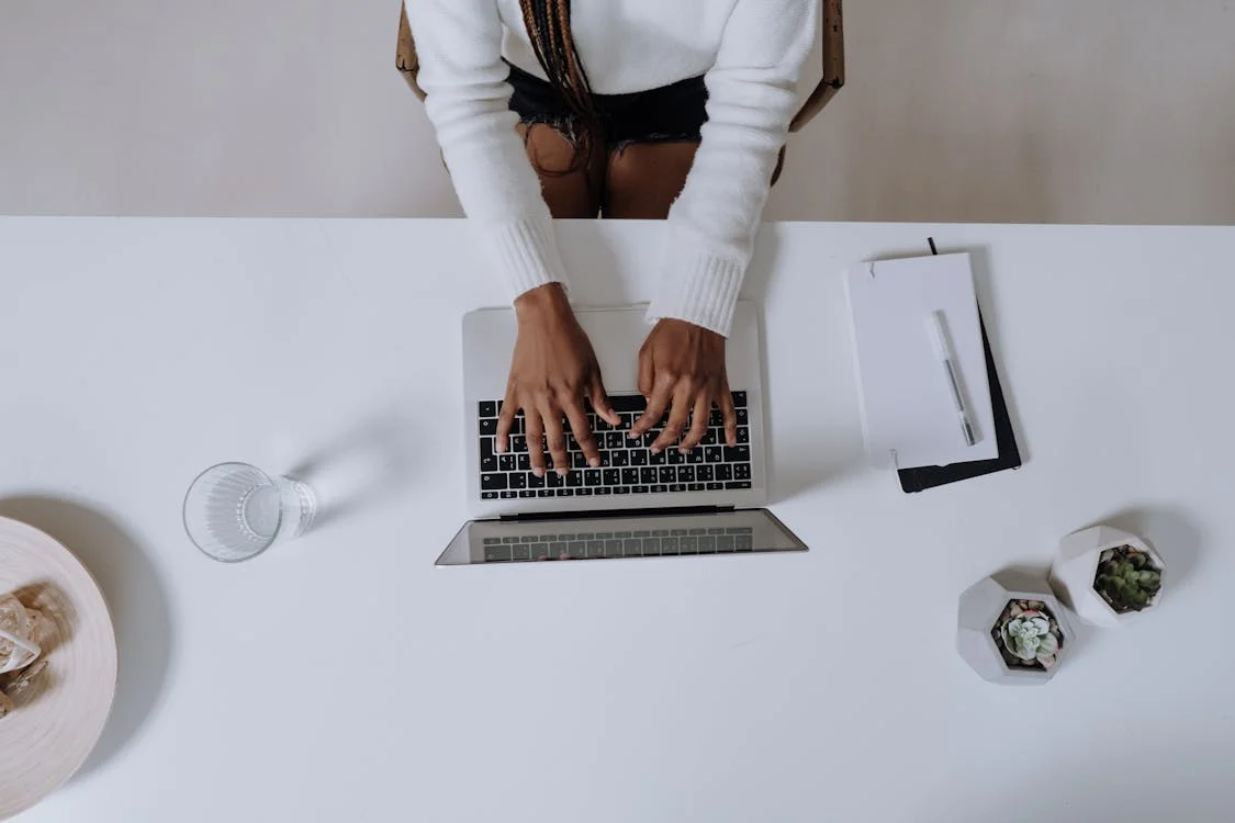 Bird’s eye view of an African-American woman in a white long-sleeve shirt working on a MacBook Pro.